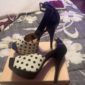 Black and white poke-a-dot 6” heels with a strap around the ankle.